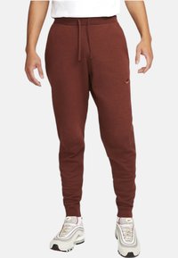 Maroon sweatpants with a drawstring waist, slim fit, and embroidered logo on the thigh, made from soft fleece material.