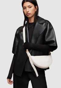 Giacca corta in pelle nera con ampi risvolti, indossata sopra un top nero a maniche lunghe. Una borsa a tracolla color crema con un design curvo e tracolla regolabile.