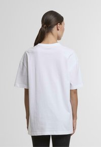 Bílý oversize bavlněný tričko s kulatým výstřihem a krátkými rukávy, má jednoduchý design a volný střih, zobrazuje zadní pohled.