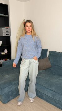 Light blue textured sweater with multicolored specks, paired with loose light denim jeans and white sneakers. Sitting on a teal couch.