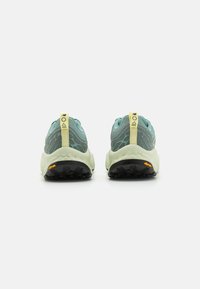 Trail running shoes with a light blue mesh upper, yellow accents, and a textured sole featuring black traction studs and an orange logo.