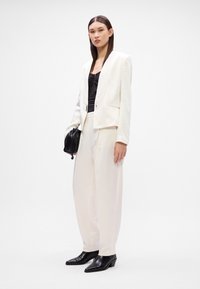 Blazer branco ajustado combinado com calças brancas largas, uma blusa preta e botins pretos de bico fino, apresentando um design minimalista.