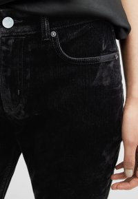 Jeans neri in velluto a coste con texture morbida, chiusura a bottone, tasche frontali e dettagli a coste verticali ben visibili. Cuciture a contrasto in evidenza.