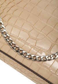 Superficie in pelle beige con motivo coccodrillo, dettagli in catena argentata trasversale e nome del marchio "Coccinelle" impresso.