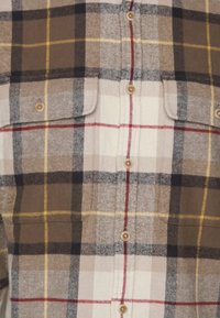 Braun-beiges karierter Flanellhemd mit zwei Brusttaschen, Knopfleiste, roten und gelben Akzenten sowie einem weichen, strukturierten Stoff.