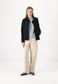 Navy trench coat with button closure, paired with a light gray crew neck sweater and beige wide-leg trousers. Black flat shoes complete the outfit.
