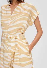 Robe à manches courtes, décolleté en V avec une taille ceinturée, présentant un motif zèbre beige et blanc et des poches latérales. Tissu texturé.
