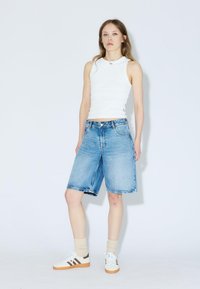 Shorts en denim bleu clair avec une coupe décontractée, avec une fermeture à bouton et un style cinq poches, associés à un débardeur blanc et des baskets.