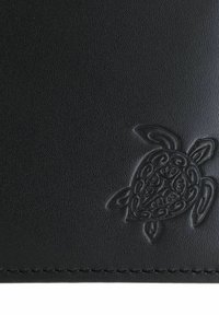 Surface en cuir noir texturé avec un motif de tortue détaillé en relief dans le coin inférieur droit au-dessus du bord cousu.