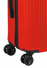 Valigia rigida rossa con design scanalato, cerniera nera e quattro ruote girevoli nere per una facile manovrabilità.