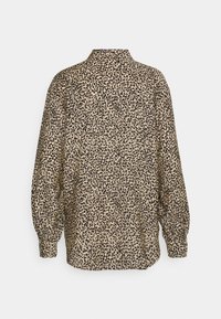 Blouse beige à manches longues avec un motif tacheté noir irrégulier, col montant et poignets boutonnés, vue de dos.