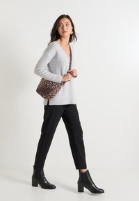 Jersey gris de punto con escote en V, combinado con pantalones negros ajustados y botas de tobillo. Se sostiene un bolso de hombro marrón con estampado de leopardo.