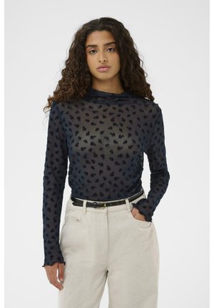 Top transparent à manches longues bleu marine avec broderies florales, col haut et poignets à volants, associé à un pantalon de couleur claire et une ceinture noire.