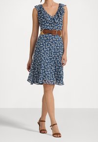 Blaues Blumenkleid mit Rüschennacken, tailliertem Schnitt und weit schwingendem Rock, kombiniert mit einem braunen Gürtel und braunen Riemchen-Heels.