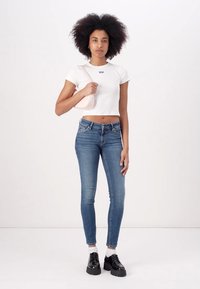 Fehér rövidített póló kis logóval, kék skinny farmernadrág, fekete platform cipő és világos rózsaszín keresztbody táska.
