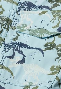 Modra jakna iz tkanine prikazuje vzorec dinozavrovih okostij v zeleni in temno modri barvi. Vključuje žep s poklopcem in gladko, sijočo teksturo.