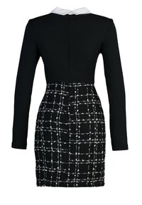 Robe noire à manches longues avec col blanc Peter Pan, taille cintrée et jupe à motif à carreaux texturés noirs et blancs.