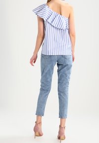 Top a righe blu e bianche con spalla scoperta e dettaglio arricciato, abbinato a jeans blu chiaro e sandali con tacco color rosa pallido.