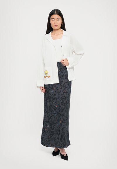 White button-up shirt with a cartoon character on the pocket, paired with a long dark skirt featuring a floral pattern, and black pointed-toe shoes.