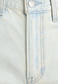 Material din denim albastru deschis cu cusături vizibile, bucle pentru curea și un nasture metalic gravat cu "Levi Strauss & Co S.F. CAL."
