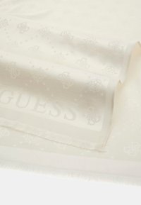 Écharpe blanche ornée d'un motif subtil de logos et d'éléments décoratifs, avec des bords frangés et une texture douce. Nom de la marque affiché de manière proéminente.