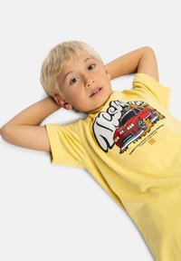Camiseta de algodón amarilla con un gráfico de un coche rojo de diseño caricaturesco, cuello redondo y mangas cortas. Textura suave.