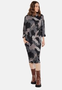 Knielange jurk in zwart en grijs abstract patroon, met een ontspannen pasvorm, collette en zijzakken. Bruine enkellaarzen completeren de look.