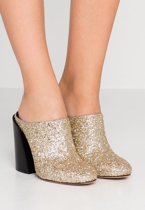 Błyszczące złote mule na wysokim obcasie z fakturowaną powierzchnią. Masywna czarna pięta stanowi kontrast dla lśniącego wierzchu.