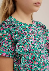 Zelený květinový top s malými růžovými a červenými květy, volánkovými rukávy a jemnou texturou, vhodný pro každodenní nošení.