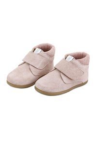 Zapatos de niña pequeños en rosa suave con tiras de velcro, puños elásticos con relieve en los tobillos y suelas de goma marrón claro sobre un fondo blanco.