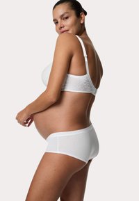 Hvid bh med blondekanter og matchende boyshorts, der har en glat stofstruktur og et sømløst design, vist på en gravid model.