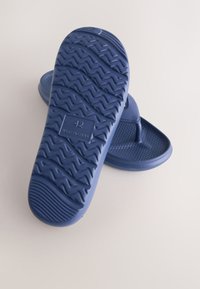 Tongs en caoutchouc bleu marine, taille 42, avec semelle texturée et bride d'orteil, une semelle face vers le haut affichant le motif de la bande de roulement et l'étiquette de taille.