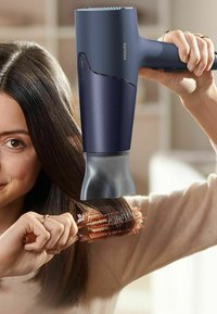 Philips haardroger met een slank donkerblauwe behuizing, ronde mondstuk en ergonomische handgreep, het stylen van haar met een ronde borstel in een lichte setting.