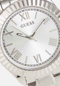 Silver stainless steel watch with a textured dial, Roman numerals, and a ridged bezel. Features include sleek hour and minute hands.