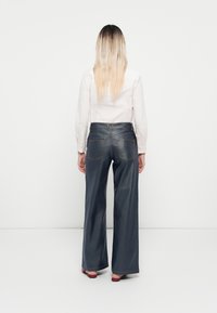 Jean large bleu foncé en denim, avec une taille haute, deux poches arrière et des coutures dorées contrastantes.