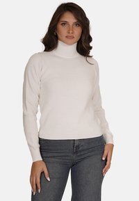 Maglione bianco a collo alto, a costine, con maniche lunghe e design aderente, abbinato a jeans in denim scuro.