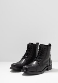 Botas de tobillo de cuero negro con punta redonda, diseño con cordones, cremallera lateral, detalles texturizados y un bajo tacón cuadrado.