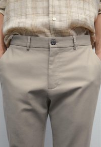 Beige bomullsbyxor med en mjuk textur, med ett standard midjeband, framfickor och en enda grå knappstängning.