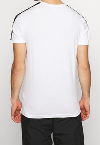 Vit kortärmad t-shirt med svarta ränder på axlarna. Tillverkad av mjukt tyg med en slät yta och en klassisk passform.