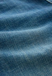 Gros plan sur un tissu en denim bleu texturé avec des détails de couture visibles et de légers plis.
