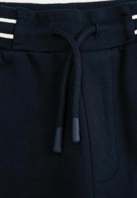 Granatowe dresy z elastycznym paskiem i sznurkiem, kontrastowe białe paski oraz miękka, teksturowana tkanina.