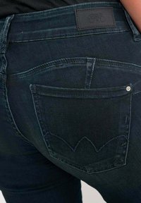 Jean en denim bleu marine avec un gros plan de la poche arrière ornée d'un design de couture pointue et d'une étiquette en cuir au-dessus.