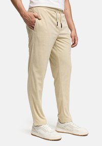 Cream corduroy joggers with an elastic waistband, side pockets, and drawstring; paired with white sneakers and a neutral t-shirt.