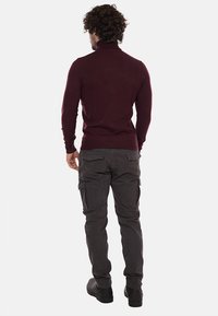 Maglione a collo alto borgogna con design aderente. Abbinato a pantaloni cargo grigi scuri con più tasche. Texture liscia, colori solidi.