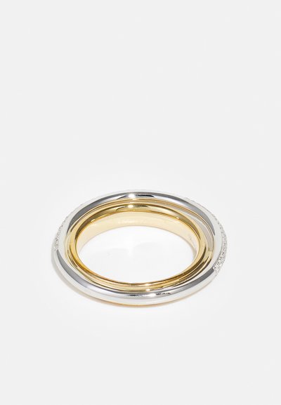 Anello interlacciato in oro e argento con finiture lisce e testurizzate, caratterizzato da un accento di diamante su un lato e un interno lucido.