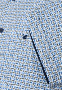 Korte mouwen shirt in blauw, groen en wit geometric patroon met donkere knoop- en trimaccenten. Katoenen stof met een gladde textuur.