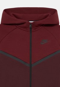 Sweatshirt Nike em cor bordeaux com fecho de correr preto, tecido bicolor, logótipo Nike preto no peito e capuz integrado.