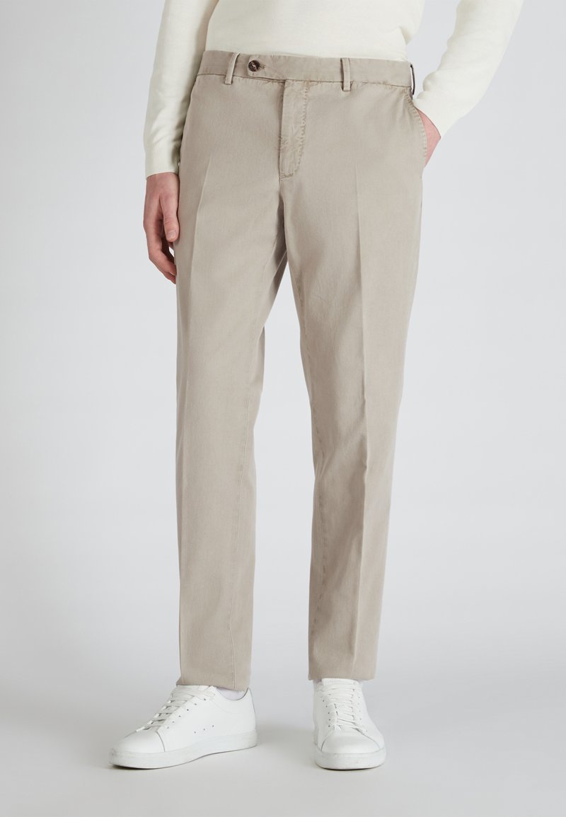 Beige op maat gemaakte broek van een gladde, licht gestructureerde stof, met een rits en een enkele knoopsluiting. Gecombineerd met witte sneakers.