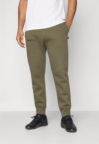 Soutiens de treino verde-oliva com um design levemente afunilado, apresentando os logótipos em preto "PARIS" e Nike, bolsos laterais e punhos canelados; tecido texturizado.