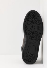 Svart och grå sneaker med en texturerad gummisula, med en cirkulär detalj nära mitten och en slät ovansida.